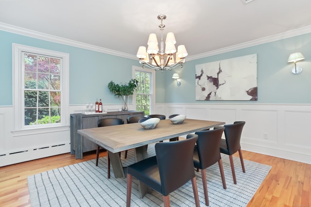 dining area featuring ornamental molding, an inviting chandelier, wainscoting, and light wood-type flooring
