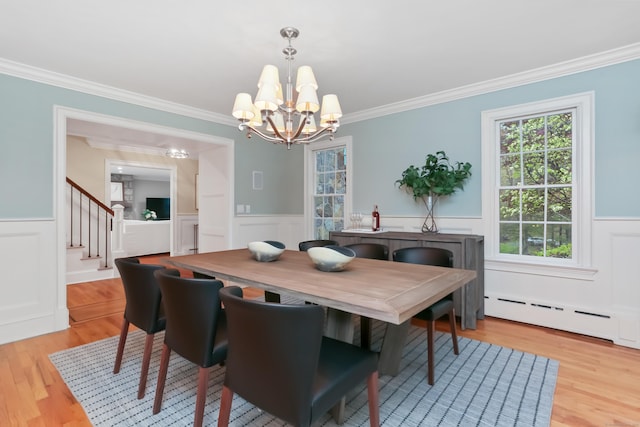 dining area with a baseboard radiator, a chandelier, wainscoting, light wood finished floors, and crown molding