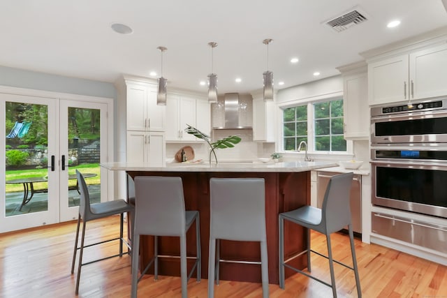 kitchen featuring double oven, white cabinetry, visible vents, light wood-type flooring, and a warming drawer
