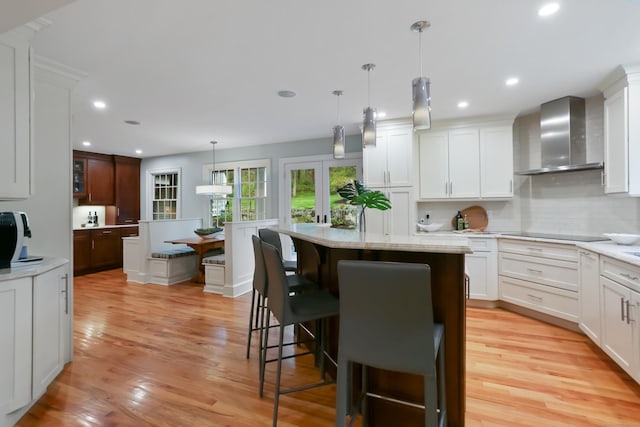kitchen featuring recessed lighting, wall chimney range hood, backsplash, light wood finished floors, and a center island