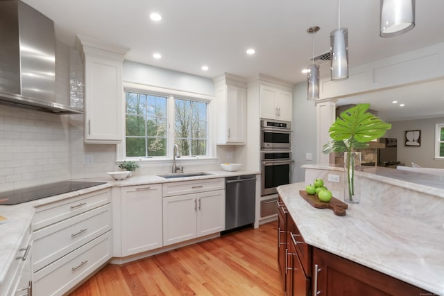 kitchen with wall chimney range hood, decorative backsplash, light wood-style flooring, a sink, and stainless steel appliances