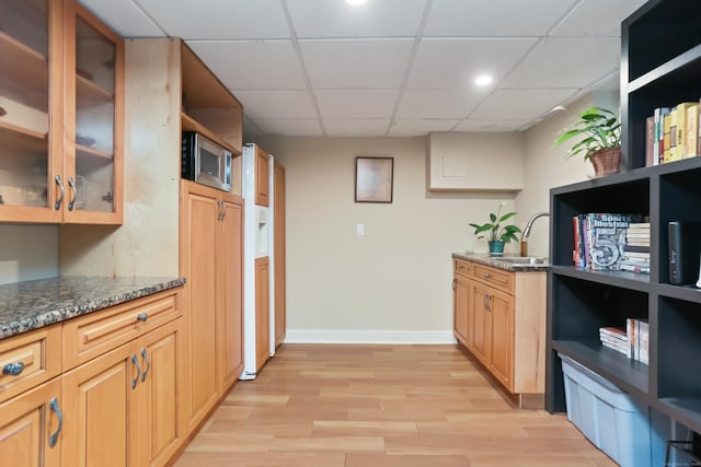kitchen with light wood-style flooring, dark stone counters, stainless steel microwave, a sink, and a paneled ceiling