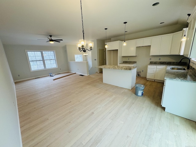 kitchen featuring white cabinets, ceiling fan with notable chandelier, light wood-type flooring, a sink, and a center island