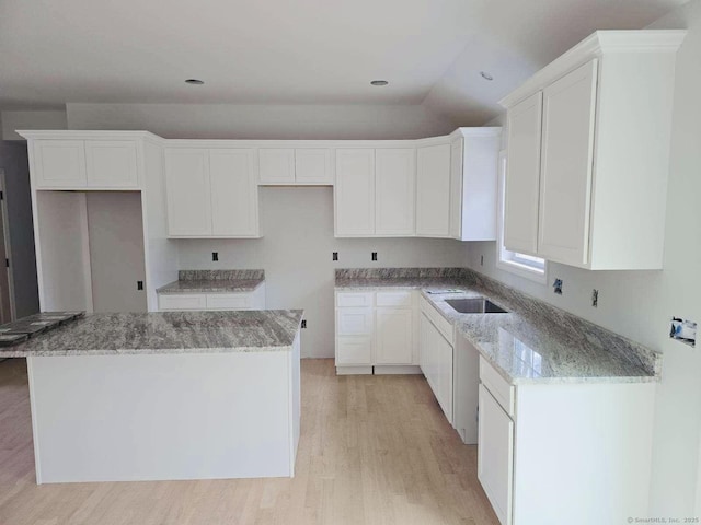 kitchen featuring light wood finished floors, a kitchen island, white cabinetry, and light stone counters