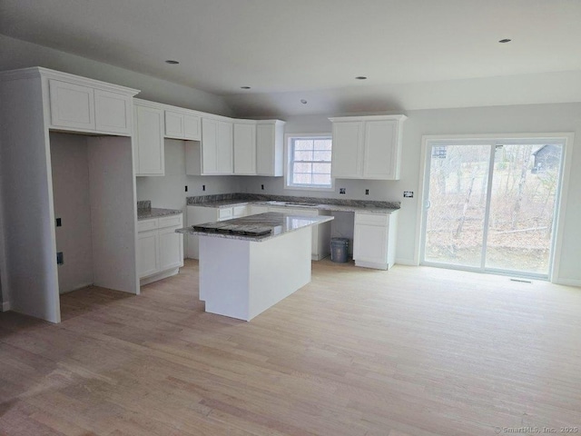 kitchen featuring vaulted ceiling, light wood-style flooring, a center island, and white cabinetry