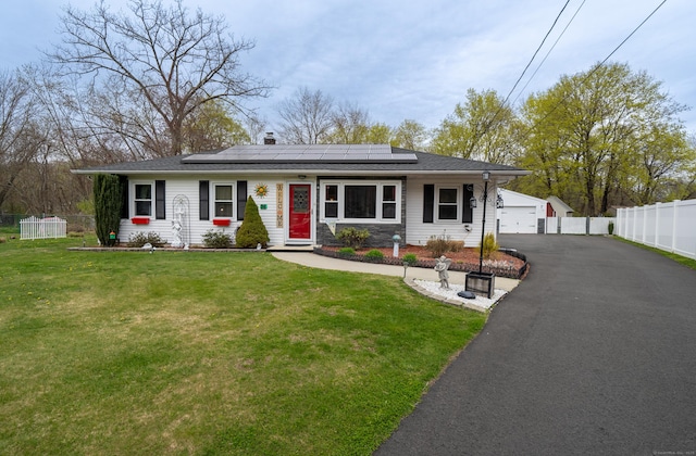 view of front of house with fence, a front lawn, and roof mounted solar panels