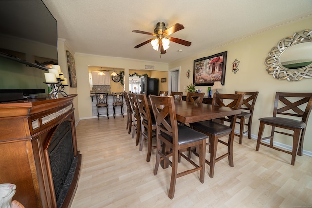 dining area with a fireplace, a ceiling fan, light wood-style flooring, baseboards, and ornamental molding