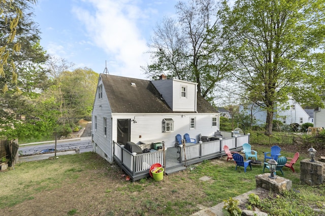 back of house with a lawn, a wooden deck, a chimney, and an outdoor fire pit