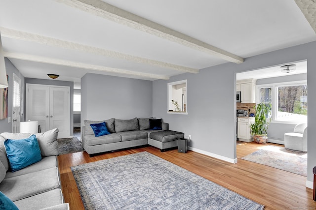 living area with beamed ceiling, a baseboard heating unit, light wood-style floors, and plenty of natural light