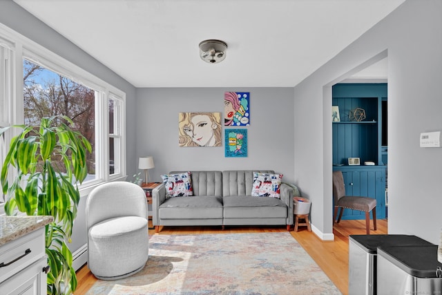 living room featuring a baseboard heating unit, baseboards, and light wood-type flooring