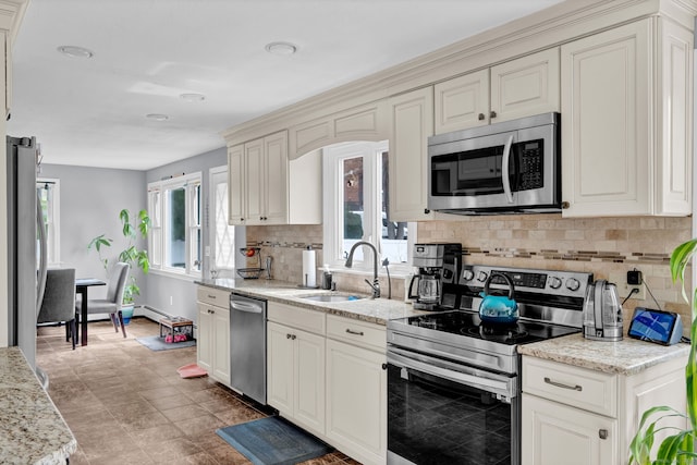 kitchen featuring light stone countertops, a sink, stainless steel appliances, cream cabinetry, and backsplash