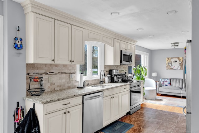kitchen featuring tasteful backsplash, stainless steel appliances, light stone countertops, and a sink
