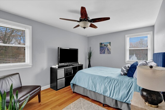 bedroom featuring light wood finished floors, multiple windows, ceiling fan, and baseboards