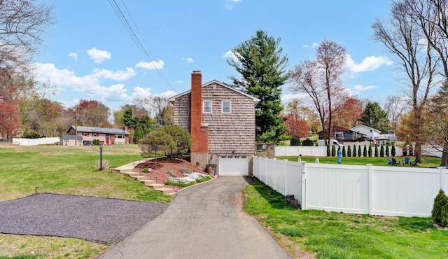 view of side of home featuring fence, a lawn, aphalt driveway, and a garage