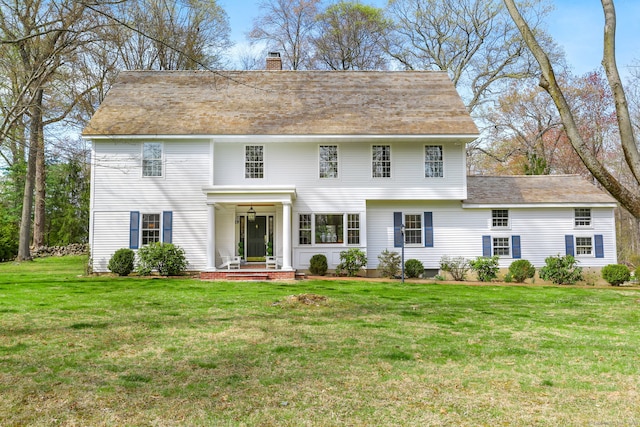 colonial home with a front lawn, a chimney, and roof with shingles