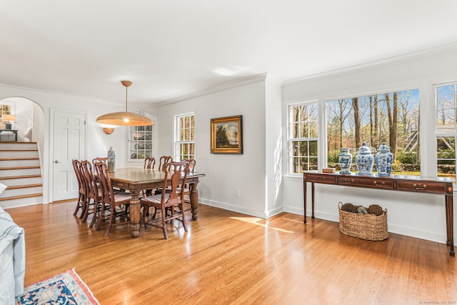 dining space featuring arched walkways, stairway, crown molding, and light wood-style flooring