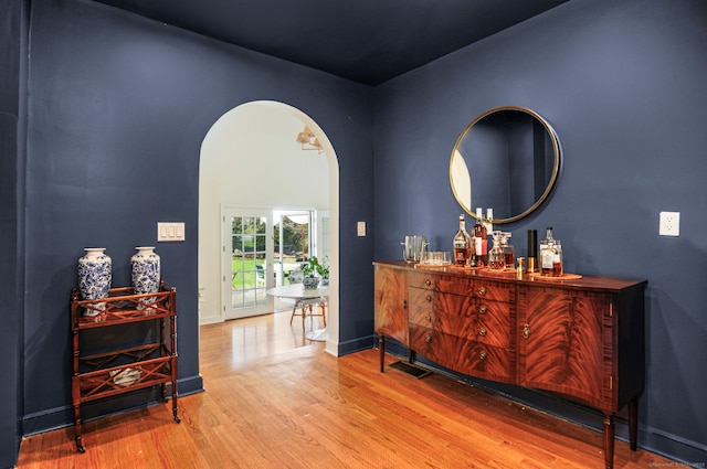 interior space with arched walkways, wood finished floors, a bar, and baseboards