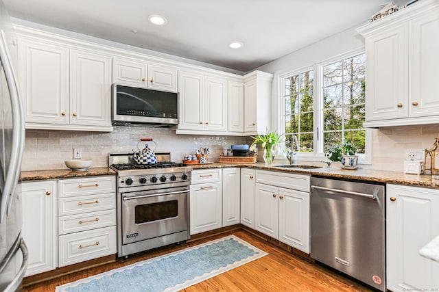 kitchen with white cabinets, stainless steel appliances, a sink, light wood-type flooring, and tasteful backsplash