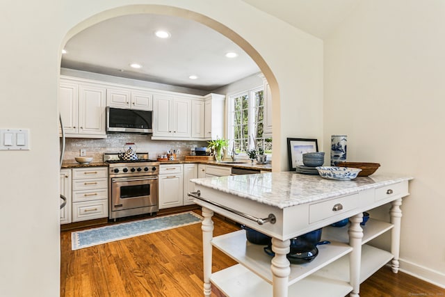 kitchen with open shelves, arched walkways, stainless steel appliances, white cabinetry, and dark wood-style floors