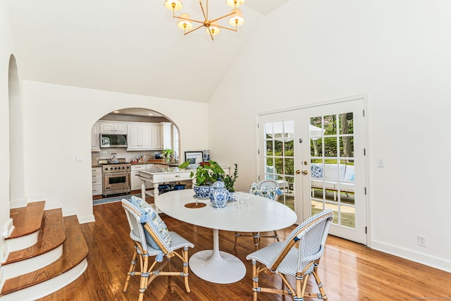 dining room with high vaulted ceiling, light wood-type flooring, arched walkways, french doors, and a notable chandelier