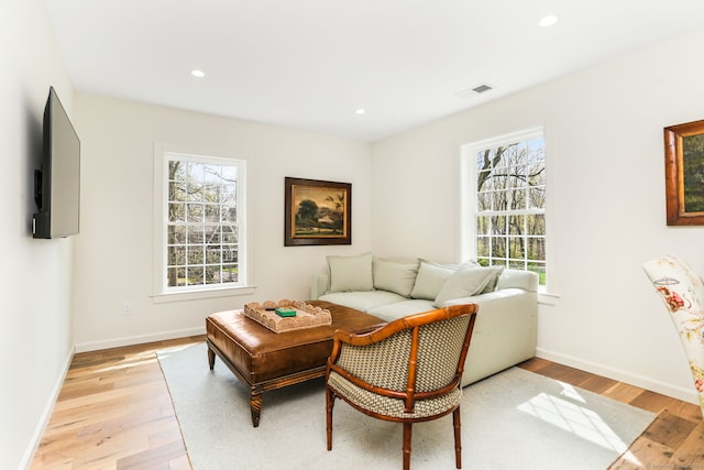 living area with a wealth of natural light, light wood-style floors, visible vents, and baseboards