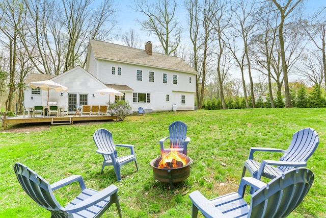back of property featuring a wooden deck, a fire pit, a chimney, and a yard