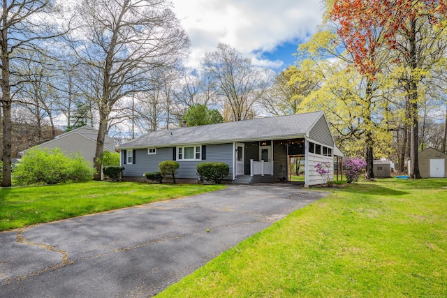 single story home featuring a storage unit, an outbuilding, a front lawn, and driveway