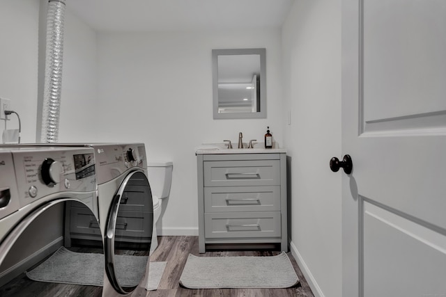laundry area with laundry area, a sink, baseboards, wood finished floors, and washing machine and dryer