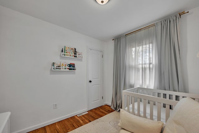 bedroom with baseboards, a nursery area, wood finished floors, and visible vents