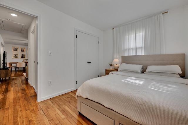 bedroom with baseboards, light wood finished floors, attic access, and a closet