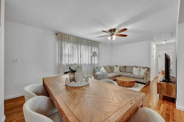 dining space featuring light wood-type flooring, a ceiling fan, baseboards, and attic access