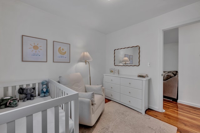 bedroom with a crib, baseboards, and light wood finished floors