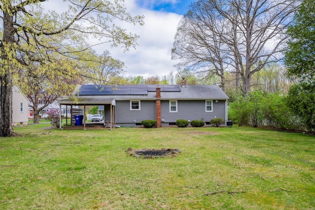rear view of property with a yard, an attached carport, solar panels, and a chimney