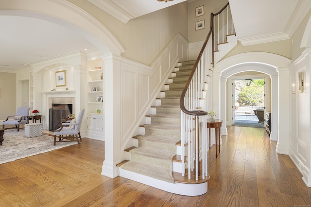foyer entrance with arched walkways, ornate columns, hardwood / wood-style flooring, a fireplace, and ornamental molding