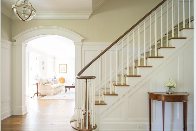 stairway with arched walkways, ornate columns, wood-type flooring, and ornamental molding