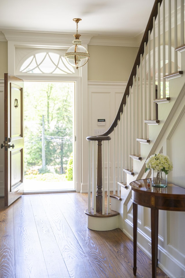 entrance foyer featuring stairway, wood finished floors, ornamental molding, a chandelier, and a decorative wall
