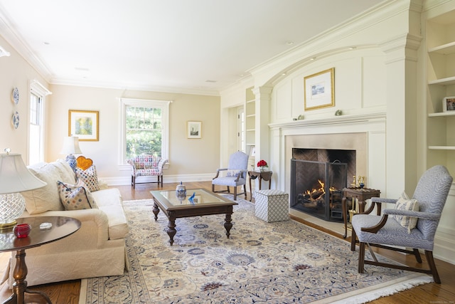 living area with wood finished floors, a fireplace with flush hearth, built in features, ornamental molding, and baseboards