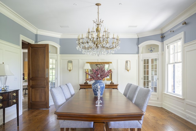 dining area featuring a chandelier, a decorative wall, hardwood / wood-style floors, ornamental molding, and arched walkways