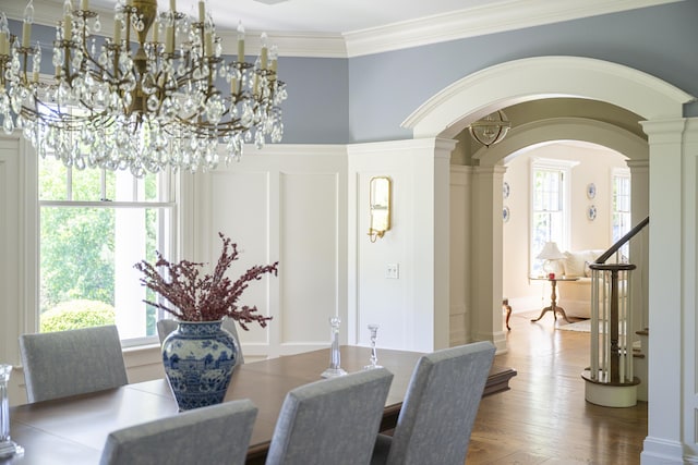 dining room featuring arched walkways, ornamental molding, a chandelier, decorative columns, and wood finished floors