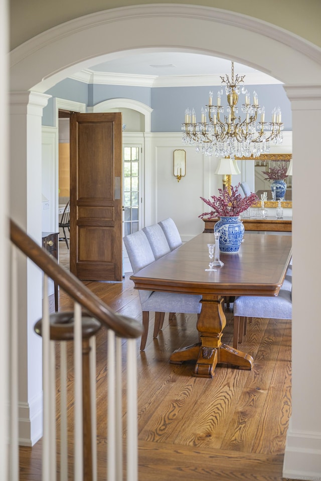dining area featuring arched walkways, wood finished floors, decorative columns, crown molding, and a chandelier