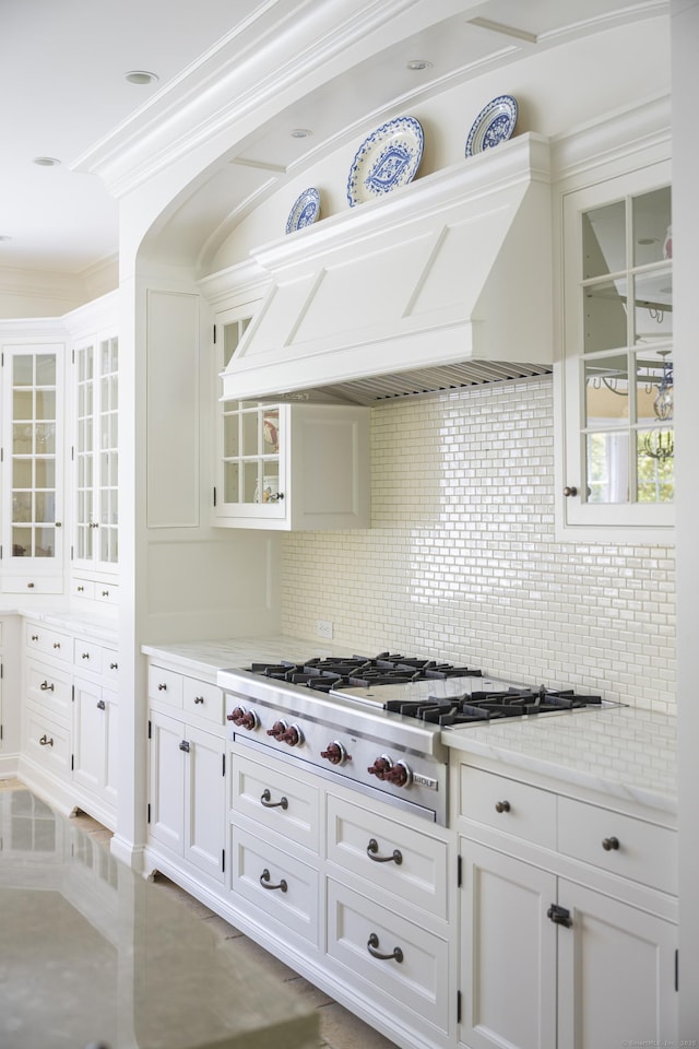 kitchen with decorative backsplash, stainless steel gas stovetop, white cabinets, glass insert cabinets, and ornamental molding