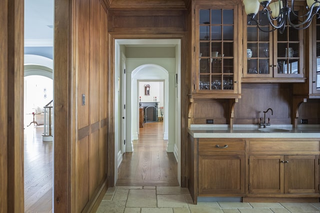 indoor bar with arched walkways, crown molding, a chandelier, and stone tile flooring