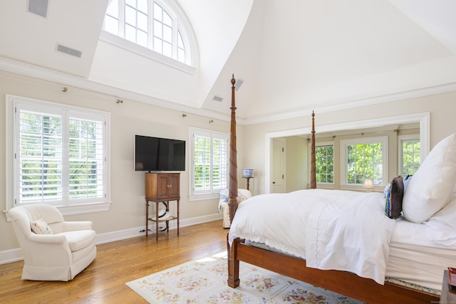 bedroom featuring a high ceiling, multiple windows, light wood-style floors, and baseboards