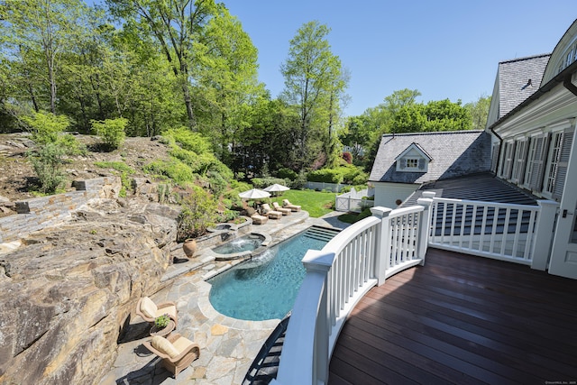 view of swimming pool featuring a wooden deck, a pool with connected hot tub, a patio, and view of scattered trees