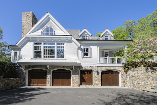 view of front of property featuring an attached garage, a balcony, asphalt driveway, a chimney, and stone siding