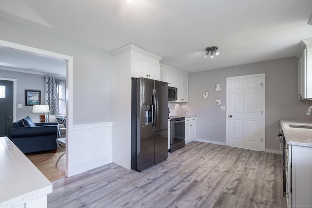 kitchen with light wood finished floors, a sink, appliances with stainless steel finishes, and white cabinetry
