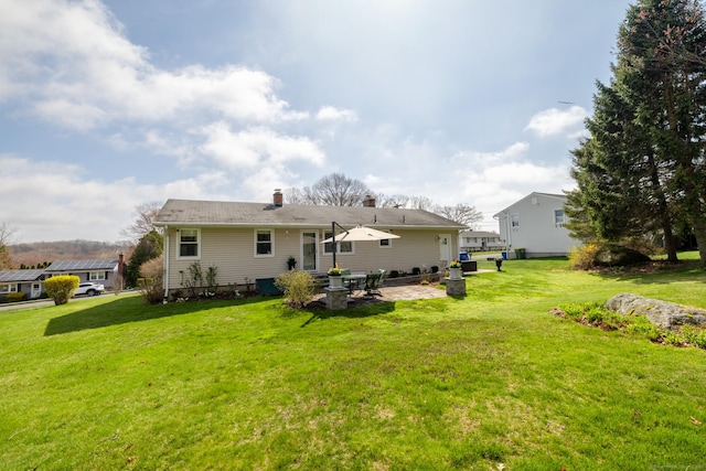 rear view of property with a chimney, a yard, and a patio area