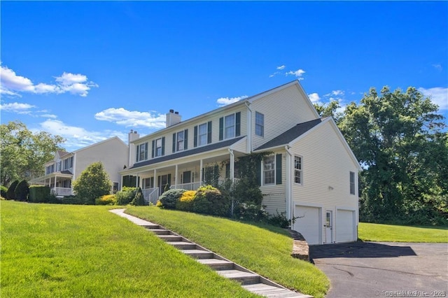 colonial home with an attached garage, a chimney, a front yard, and aphalt driveway
