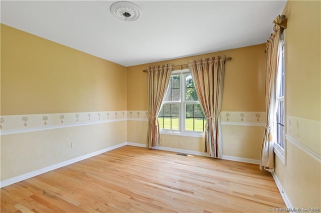 unfurnished room featuring visible vents, light wood finished floors, and baseboards