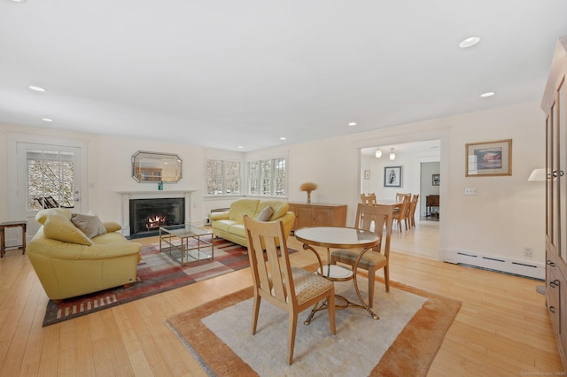 dining room featuring baseboard heating, recessed lighting, a lit fireplace, and light wood-style flooring